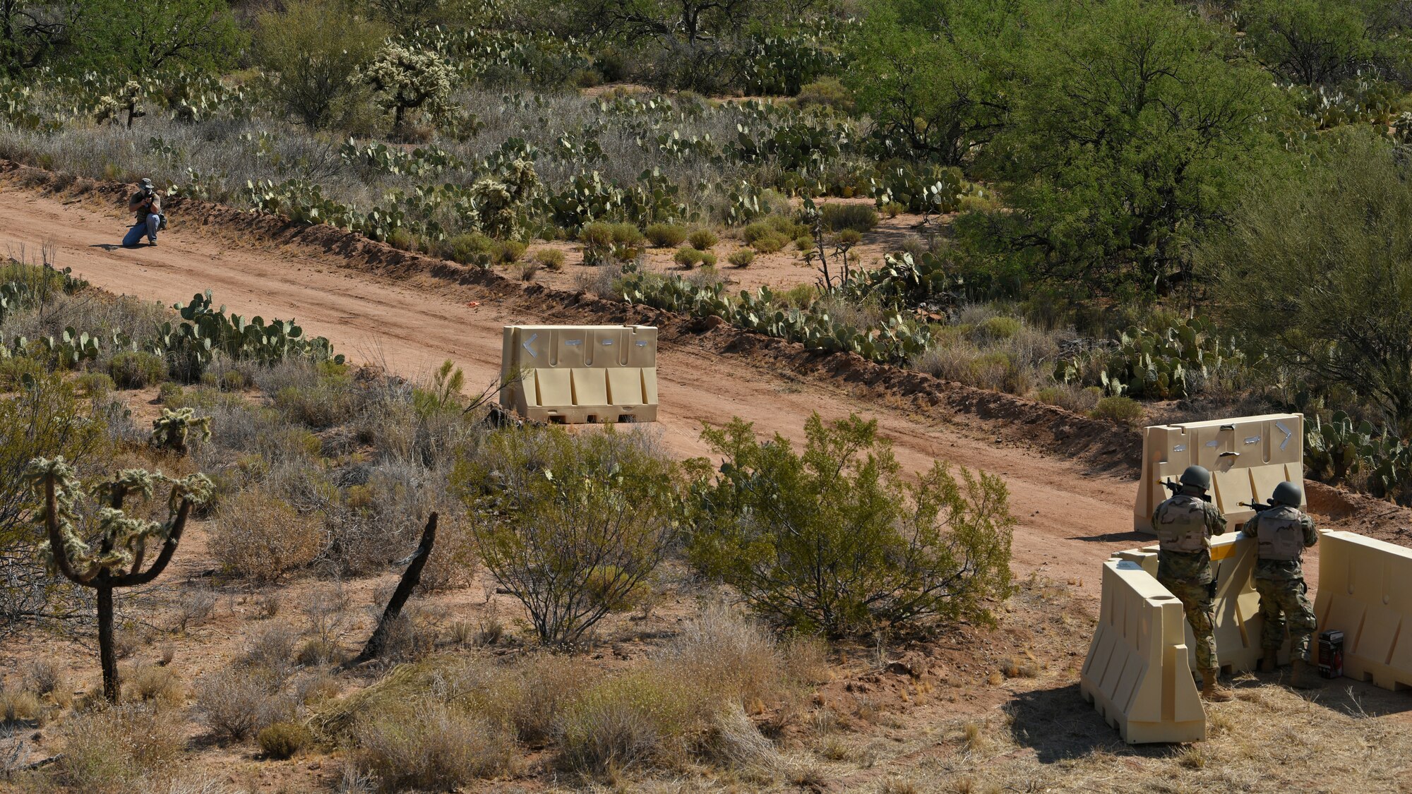 Air Force Airmen behind a defensive fighting position barrier engage in simulated weapon fire exchange with a simulated adversary in an austere location