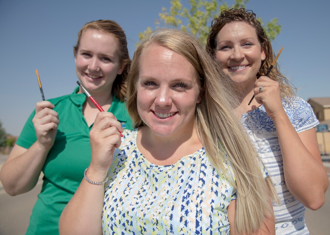 (from left to right) Kim Furry, 49th Force Support Squadron community activity center manager, Jackie Ottesen, 6th Attack Squadron key spouse, and Maj. Naomi Donovan, 924th Aircraft Maintenance Squadron commander and 2018 49th Mission Support Group key spouse, pose for a photo holding paint brushes, June 23, 2020, on Holloman Air Force Base, N.M. Holloman key spouses paint this decorative rock approximately every two weeks to highlight fun events, holidays and general base awareness activities in order to promote community, cohesion and aid in putting a smile on Team Holloman members’ faces. (U.S. Air Force photo by Senior Airman Collette Brooks)