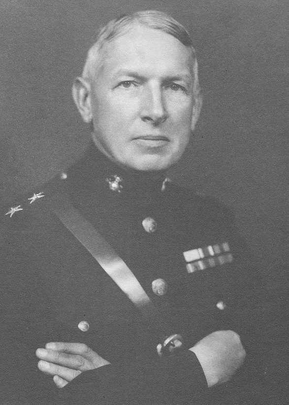 A young man wearing a dress uniform poses for a photo with his arms crossed on his chest.