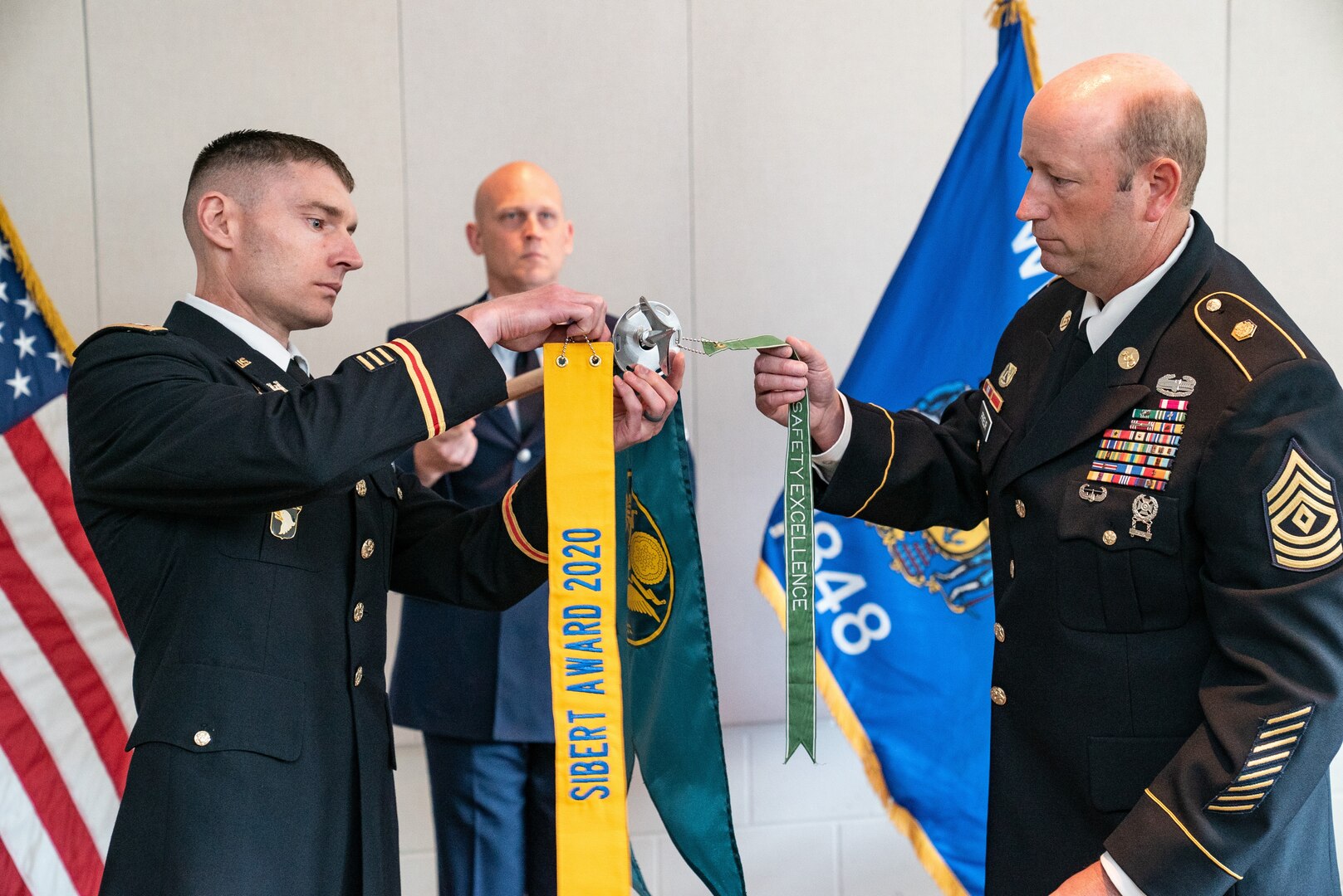 Lt. Col. Joseph Davison, left, and 1st Sgt. Kenneth Prieur, commander and first sergeant of the Wisconsin National Guard's 54th Civil Support Team, attach the 2020 Maj. Gen. William L. Sibert Award streamer to the unit's guidon during a June 23, 2020, virtual U.S. Army Chemical Corps ceremony. The U.S. Army Chemical Biological Radiological and Nuclear (CBRN) School annually presents the Sibert Award to the top CBRN units in the active component, Army Reserve, and Army National Guard.