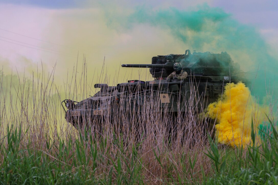 Soldiers in a tank ride through yellow and green smoke.