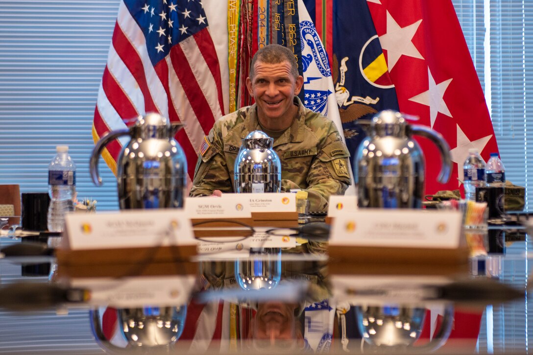 Sergeant Major of the Army sits a table with flags in the background.