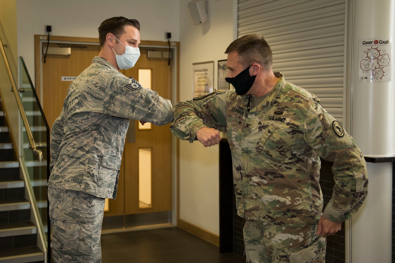 An airman and a soldier, both wearing face masks, exchange an elbow bump during an awards ceremony.