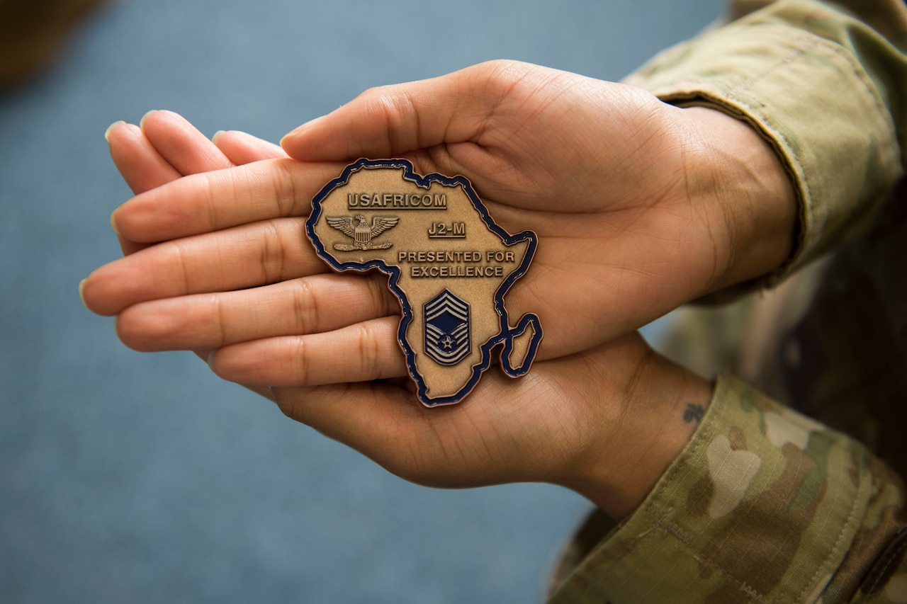 Hands hold a large recognition coin in the shape of the African continent and inscribed for excellence on behalf of U.S. Africa Command.