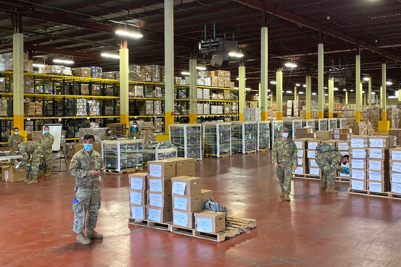 Soldiers work in a warehouse among many pallets bearing cardboard boxes.