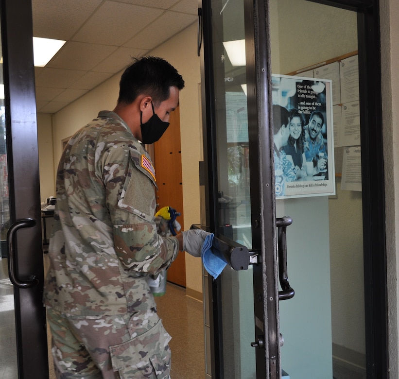 A soldier wearing a mask cleans a door handle.