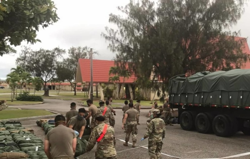 Soldiers transfer duffel bags lined up on the ground into a truck.