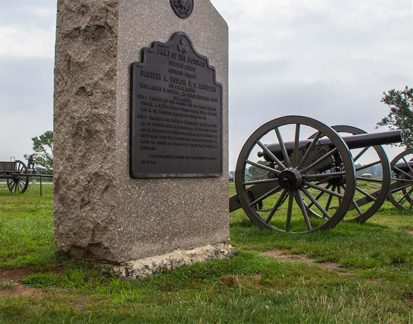 A large monument sits in grass beside three cannons.