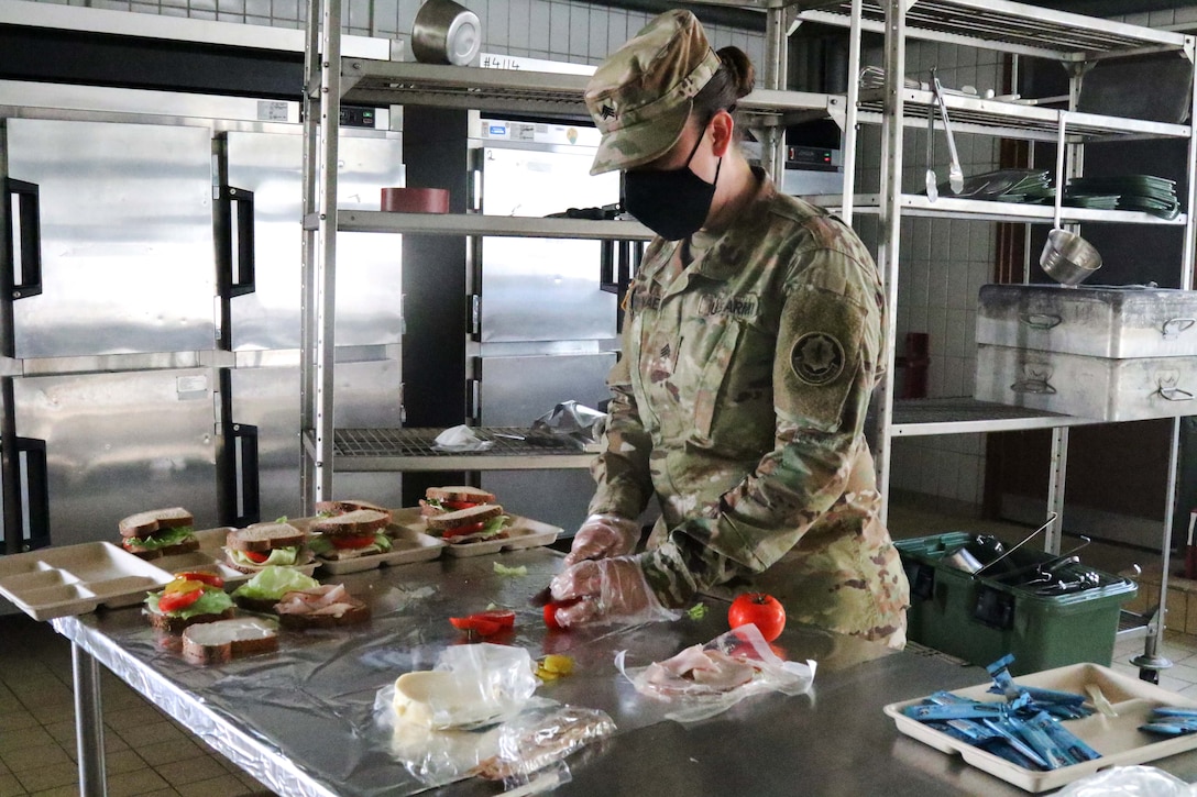 A soldier wearing a mask and gloves prepares meals.