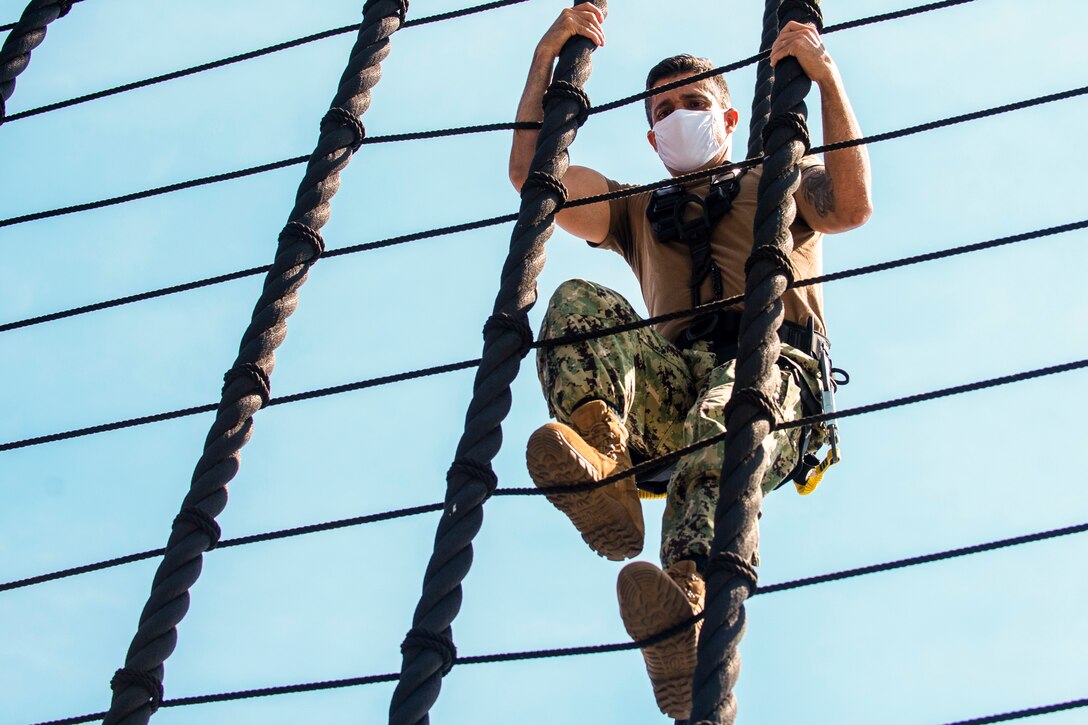 A sailor in protective gear climbs ropes.