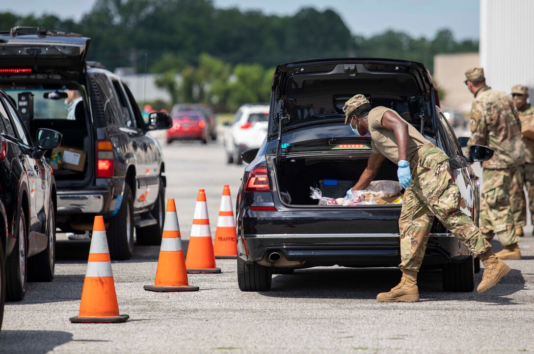 A guardsman places food in the trunk of a car.