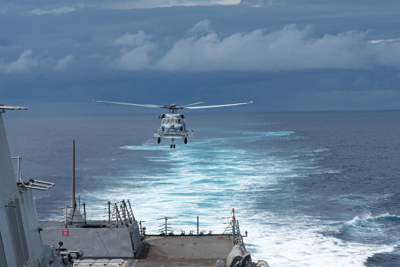 A helicopter prepares to land on a ship.