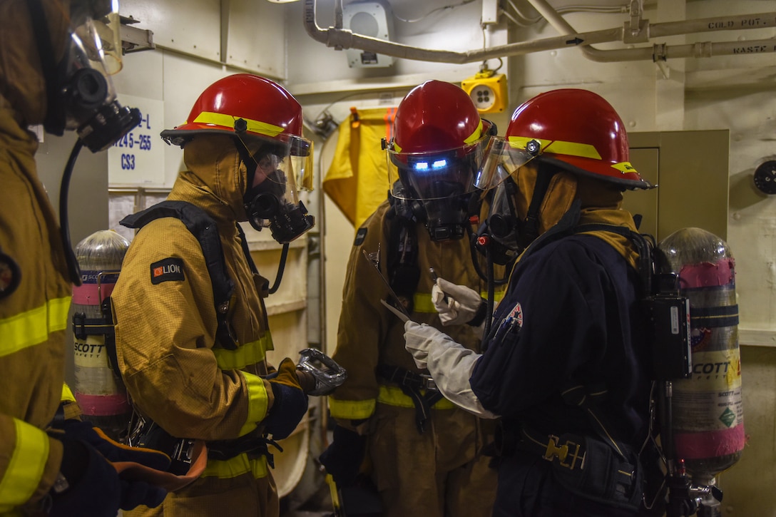 Four sailors look over a document on a ship.