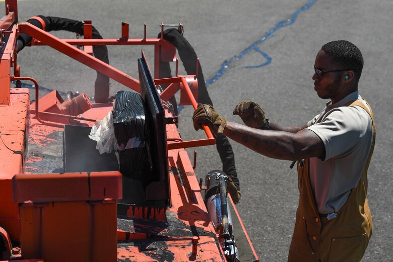 Senior Airman Irvin Matthews, 627th Civil Engineer Squadron pavements and construction equipment technician, dumps a bag of solid tar into a tar kettle to prepare it for use after completing resealing for the day on the McChord Field flight line on Joint Base Lewis-McChord, Wash., June 25, 2020. The tar kettle heats up to about 475 degrees farenheit to keep the tar in a liquid state and ready to dispense. (U.S. Air Force photo by Airman 1st Class Mikayla Heineck)