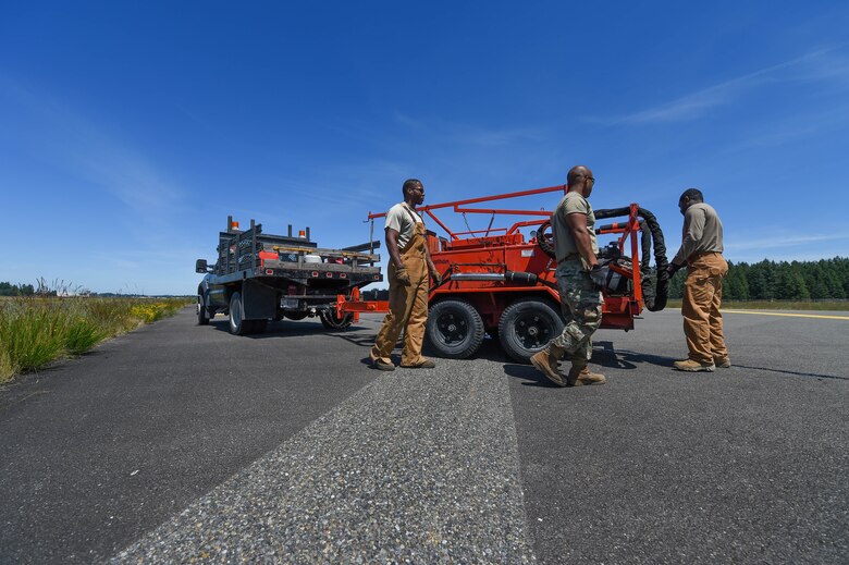 Senior Airman Irvin Matthews, left, Airman 1st Class Felipe Reyes-Cedeno, middle, and Staff Sgt. Adrian Carter, right, 627th Civil Engineer Squadron pavements and construction equipment technicians, secure a tar kettle and dispensing hose to drive back after finishing the resealing of several cracks in the asphalt of the McChord Field flight line on Joint Base Lewis-McChord, Wash., June 25, 2020. Resealing the cracks in the flight line prolongs its life by preventing erosion and is a faster method than replacing entire sections of asphalt. (U.S. Air Force photo by Airman 1st Class Mikayla Heineck)