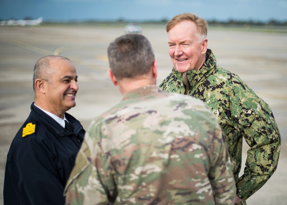 Three men in uniform meet on a flightline.