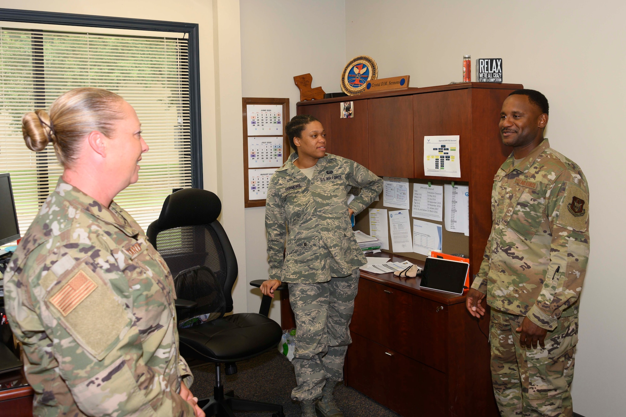 Three Airmen stand in an office, talking.