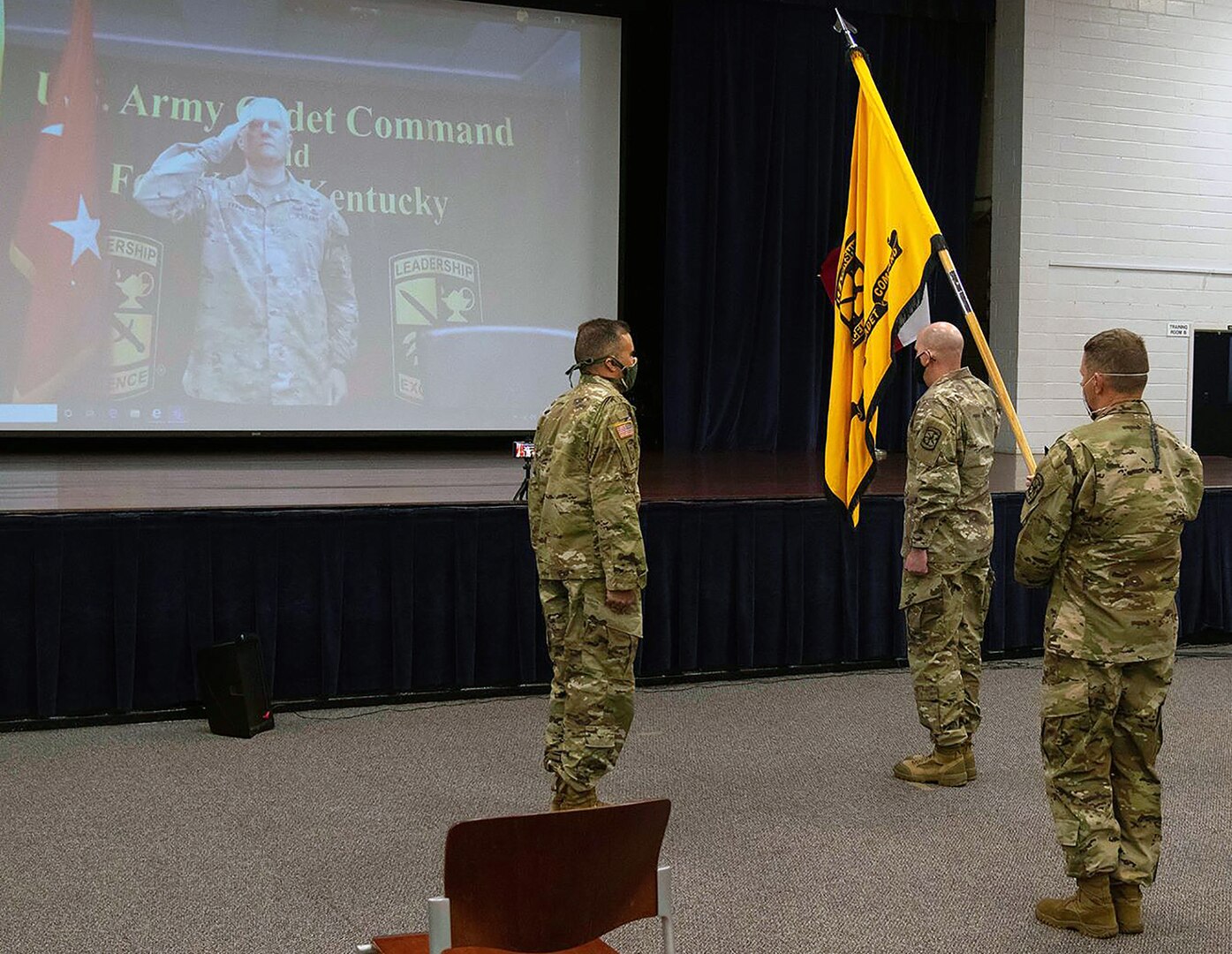 Col. Chris S. Alfeiri (right), departing 5th Brigade commander, salutes Maj. Gen. John R. Evans Jr. (on screen), commanding general, U.S. Army Cadet Command, while Col. Mark A. Olsen, incoming commander (left), looks on June 23.