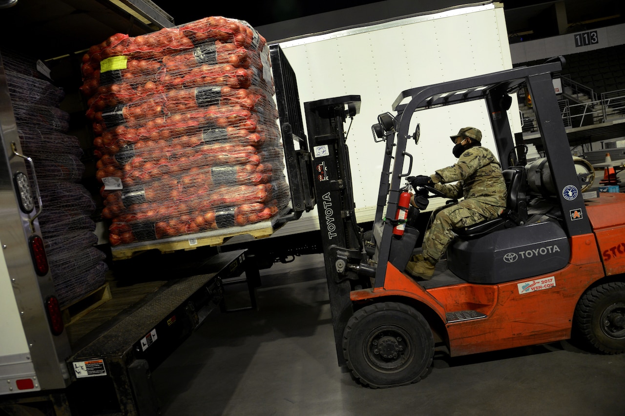 A soldier uses a forklift to lift a pallet of food.