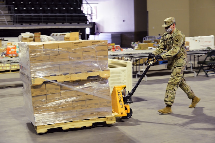 A soldier uses a portable forklift to move a pallet of food.