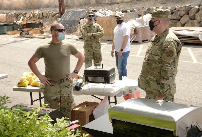 Guardsmen wearing face masks stand next to a table with food on it.
