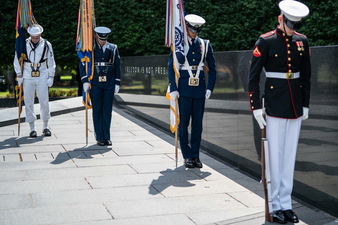Four members of the military bow their heads during a ceremony at a memorial.