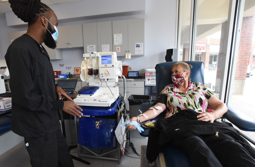 A technician speaks with a woman lying on a blood-donation table with a catheter in her arm.