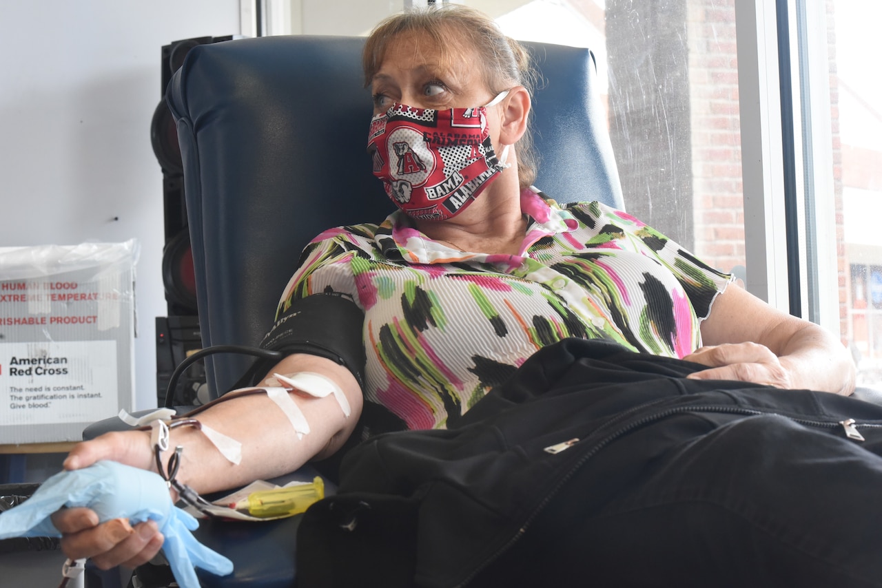 A woman wearing a face mask lies on a table with a catheter in her arm.