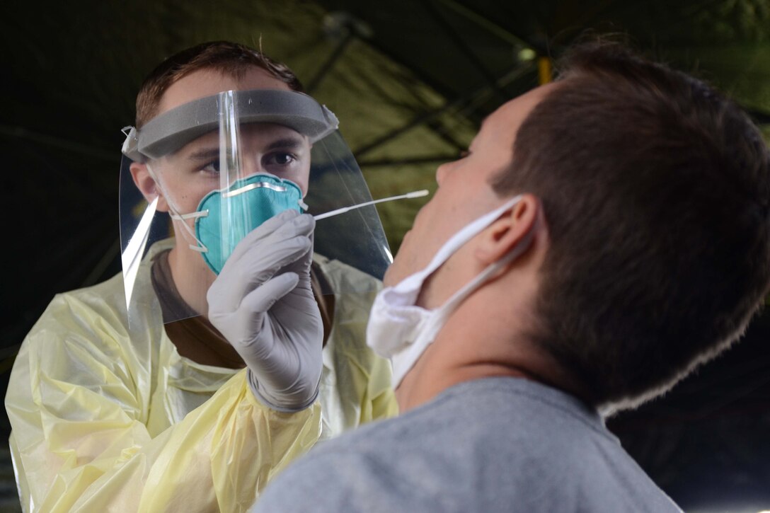A man in a medical uniform swabs inside another man's nose.