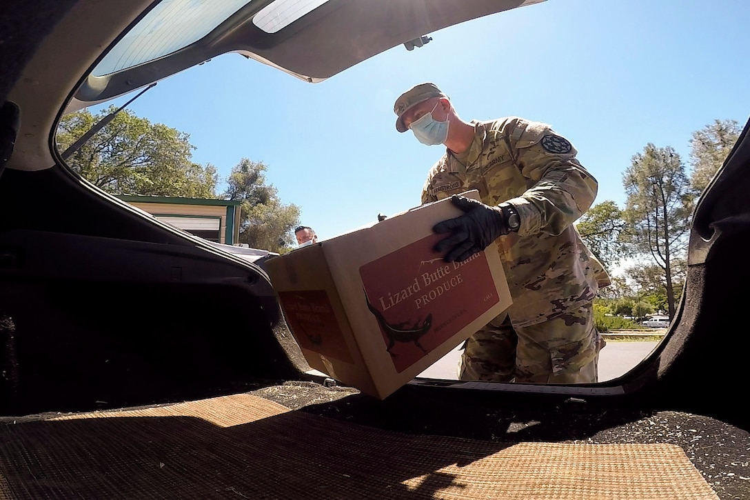 A guardsman wearing protective gear puts a box into a vehicle.