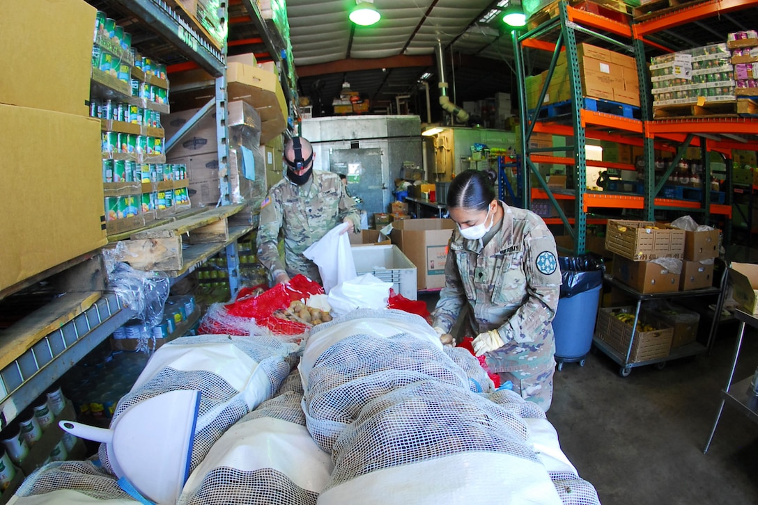 Two National Guardsmen bag potatoes in a food bank.