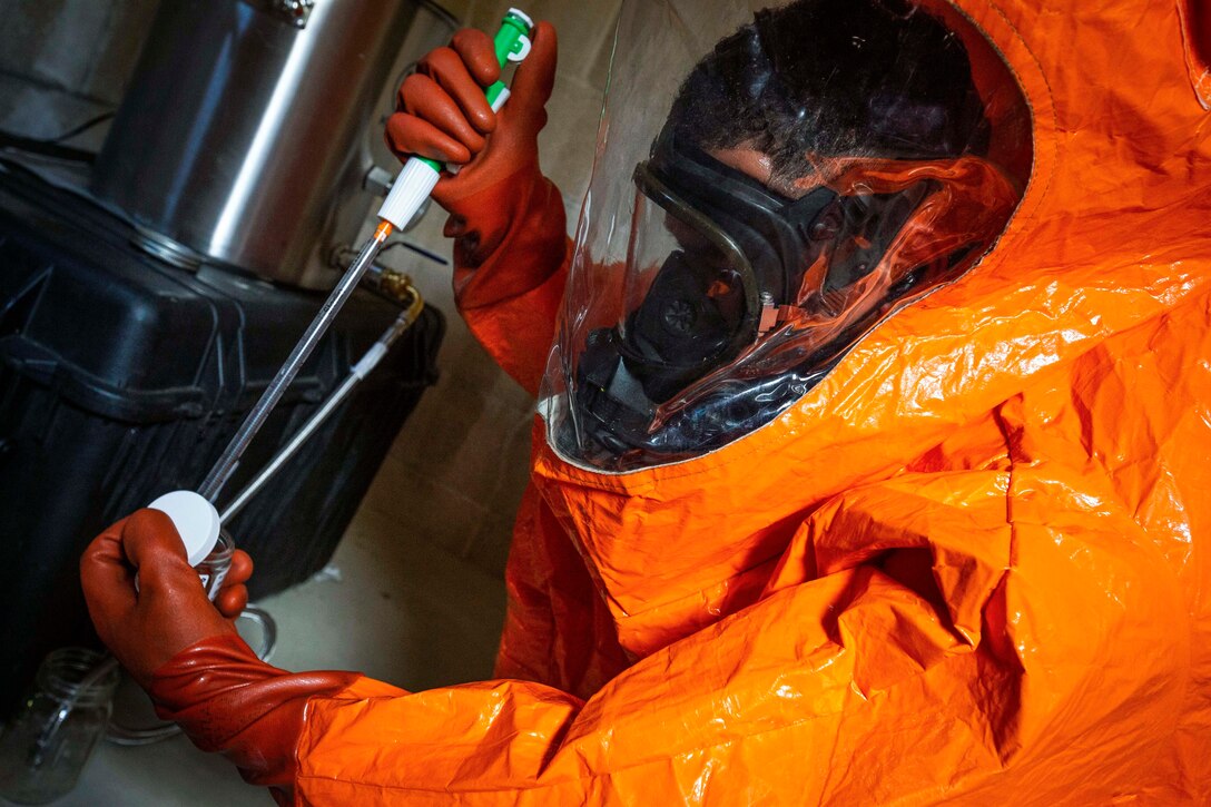 A guardsman in an orange protective suit puts an item into a container.