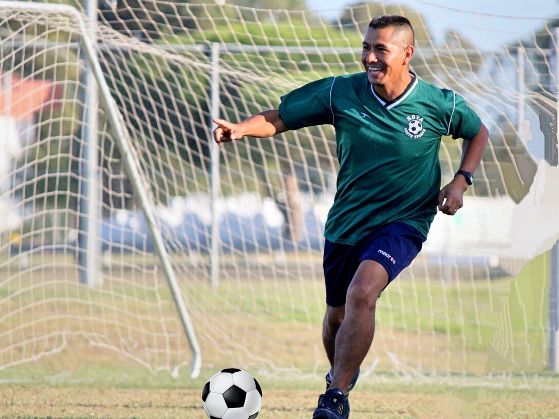 A man dressed in a soccer uniform runs toward a soccer ball on a field.