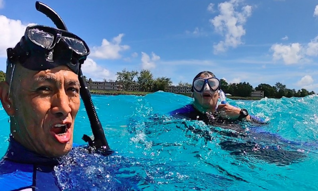 Two people snorkel in clear, blue water with the shoreline in the background.