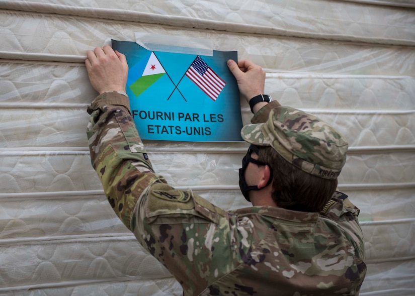 A soldier hangs a sign that bears the flags of the United States and DJibouti.