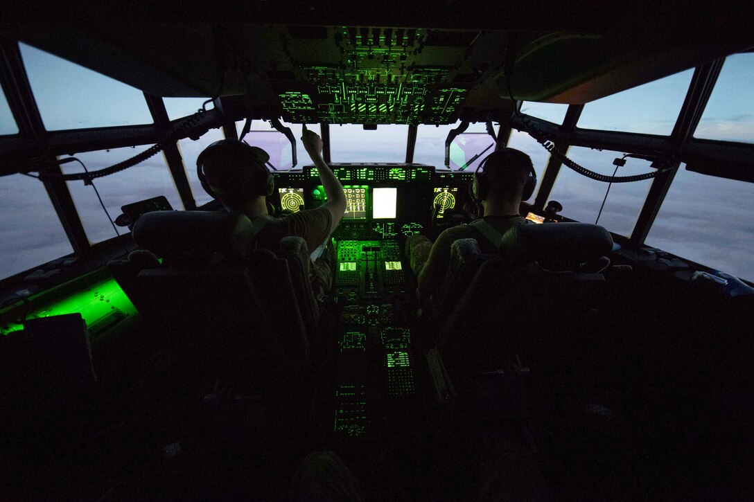 Two pilots and an aircraft cockpit are bathed in green light.
