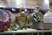 Alaska Army National Guard Soldiers Sgt. Kekoa Maclovesramirez and Staff Sgt. Edward Jones, assigned to the AKARNG Recruiting and Retention Battalion slice cucumbers for pre-packed lunches in the kitchen at Bean’s Cafe in Anchorage, Alaska, Apr. 8, 2020. This food will be distributed to thousands of local Alaskans sheltering at Sullivan and Boeke arenas as well as the Alaska After School Lunch program. (U.S. Army National Guard photo by Sgt. Seth LaCount/Released)
