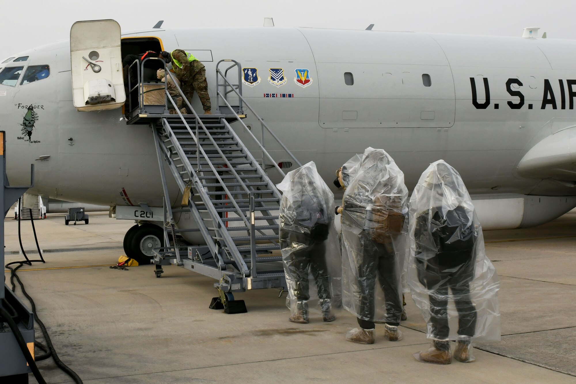Photo shows Airmen lined up at foot of stairs waiting to board an aircraft.