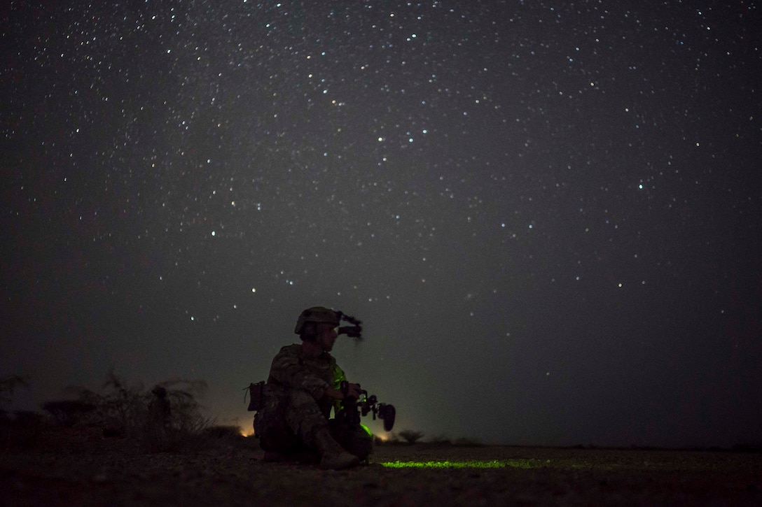 An airman kneels on the ground on a starry night.