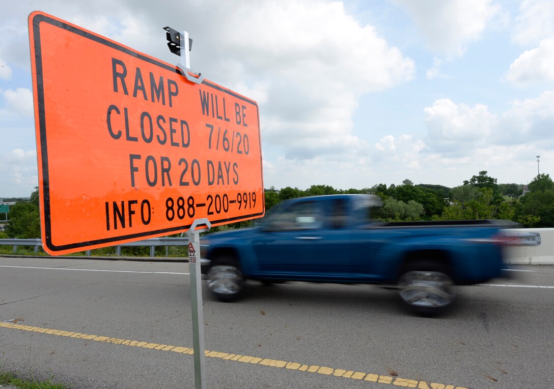 A blue truck driving by a an orange rectangle sign that say "RAMP WILL BE CLOSED 7/6/20 FOR 20 DAYS INFO 888-200-9919 in black letters.