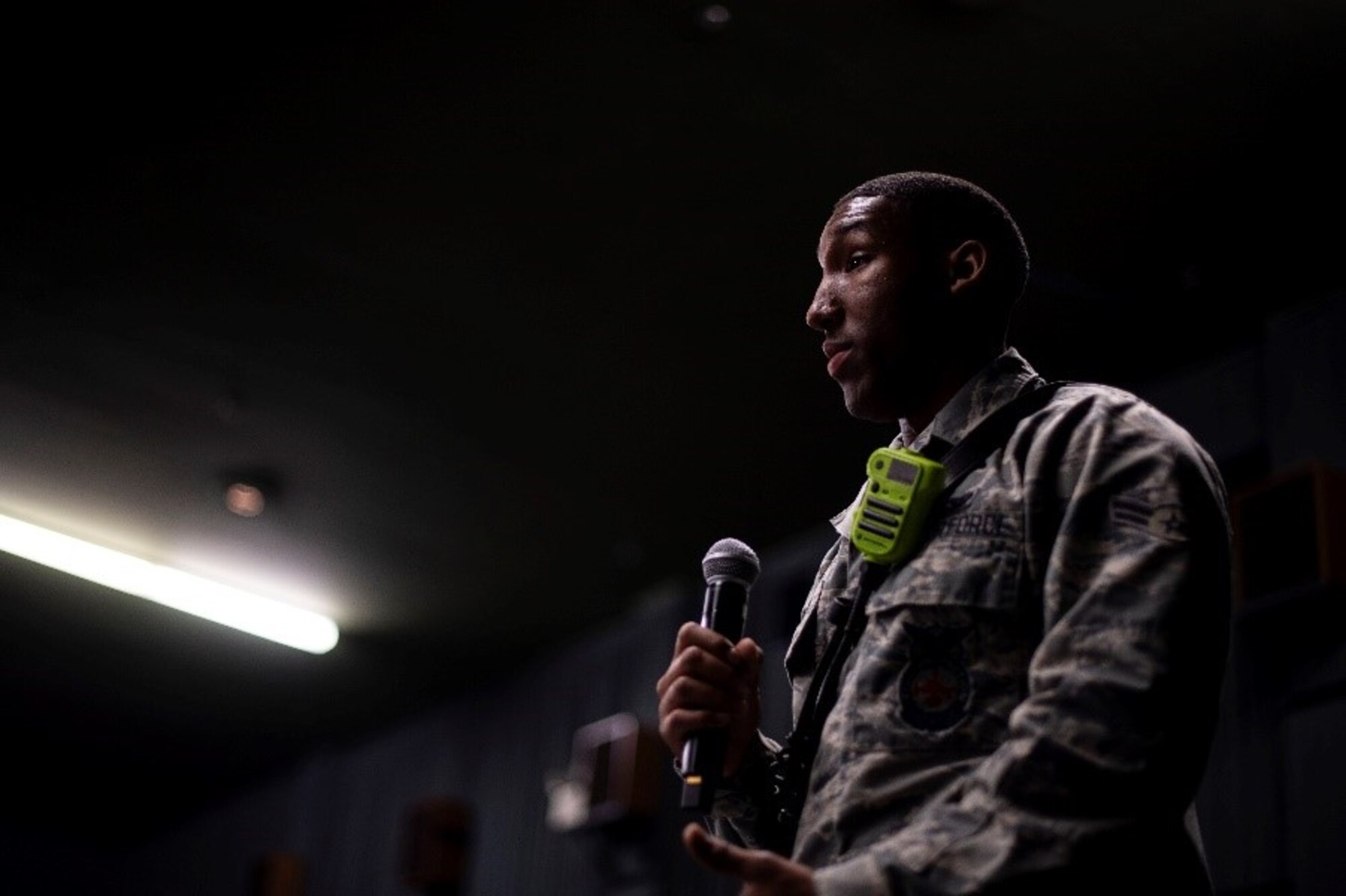 A man in a military uniform holds a microphone while he speaks to an audience off screen.