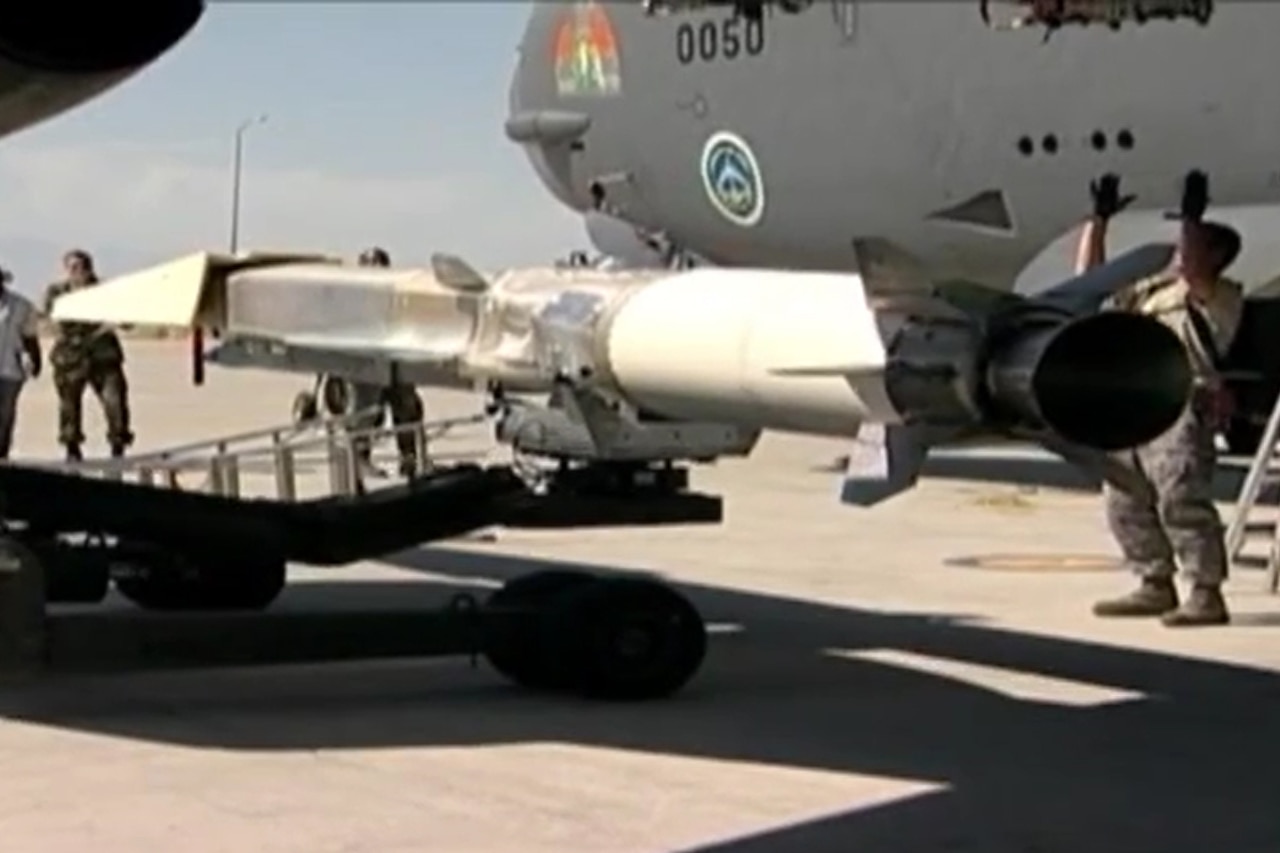 A small, dart-like aircraft is lifted into position below the wing of a much larger aircraft.