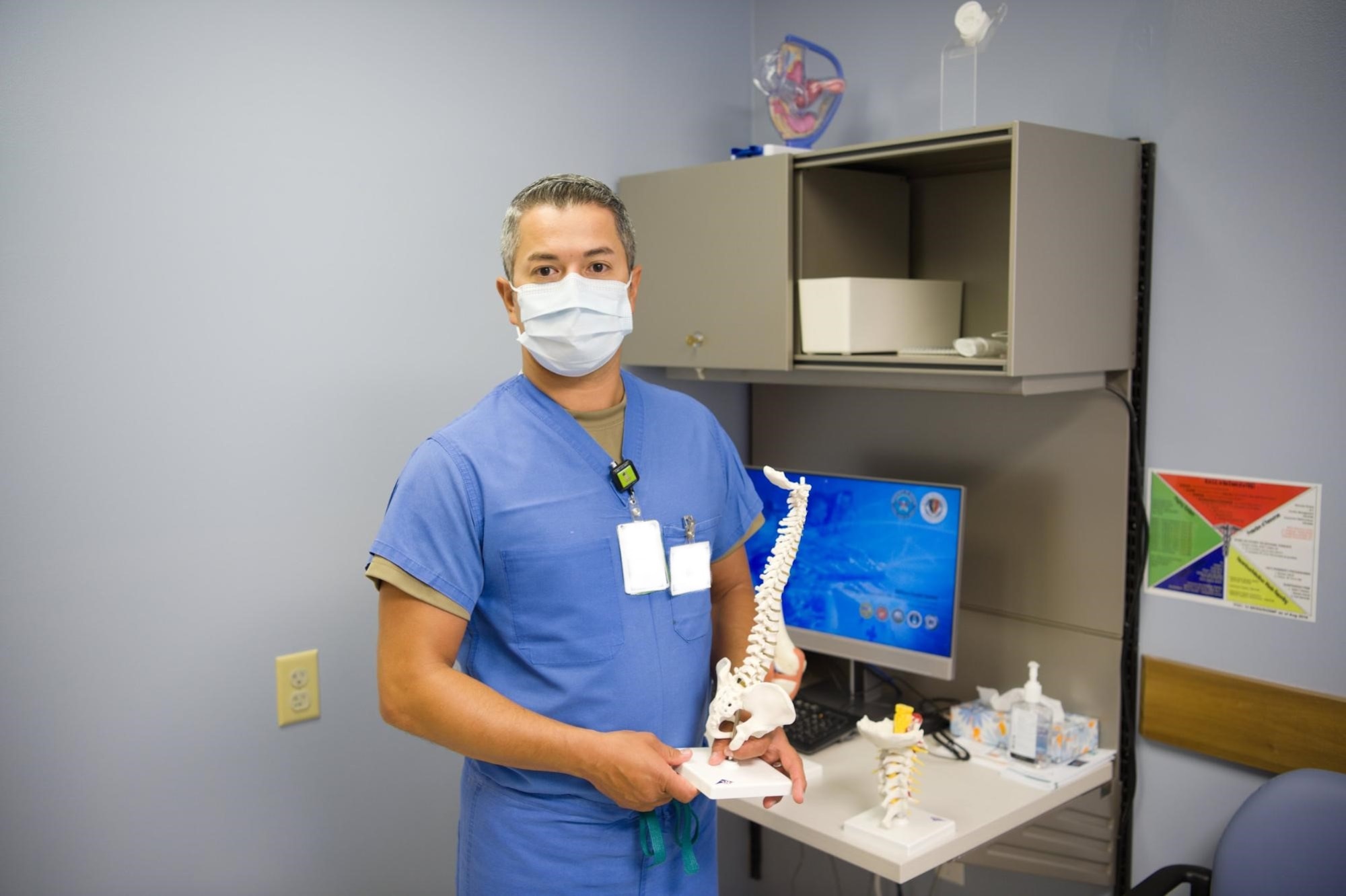 Capt. Juan Moreno, 15th Medical Group Active Duty Clinic physician assistant, holds a model of the human spine, to bring awareness to the musculoskeletal problems men face at Joint Base Pearl Harbor-Hickam, Hawaii, June 25, 2020. The 15th MDG provides both in-person and virtual medical appointments to Airmen during the COVID-19 pandemic and can assist with men’s health issues. (U.S. Air Force Illustration by 2nd Lt. Benjamin Aronson)