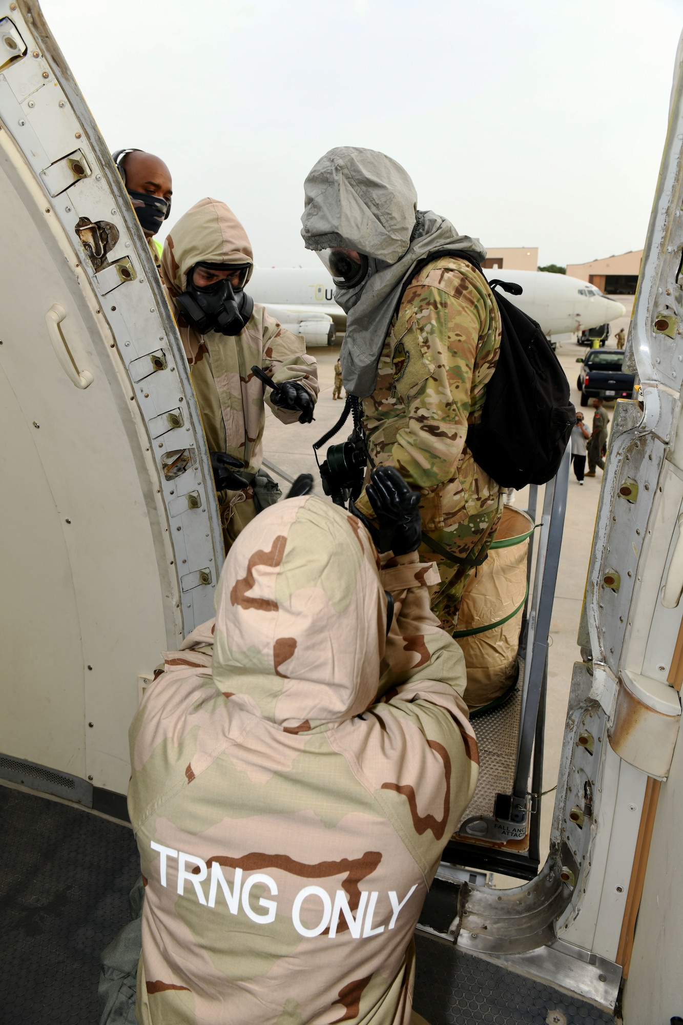 Photo shows Airmen helping someone in CBRNE gear maneuver onto an aircraft.