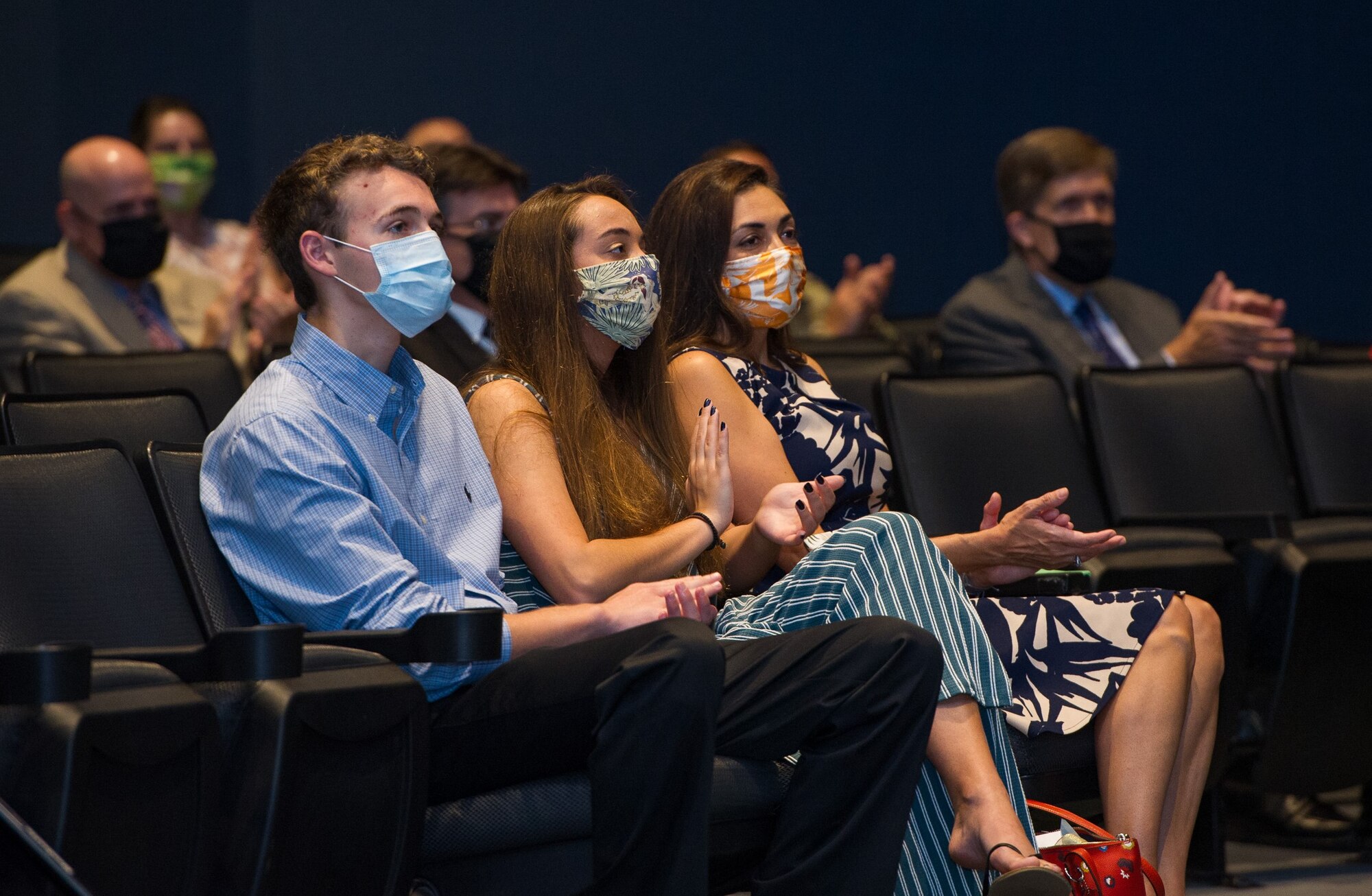 Donned in protective facial masks in the wake of the coronavirus pandemic, Gina Hartman (right) and her children Logan (left) and Sofia (center), applaud during the Air Force Technical Applications Center’s Change of Command ceremony June 30, 2020.  Gina’s husband, Col. Chad Hartman, relinquished command of the nuclear treaty monitoring center to Col. Katharine Barber at Patrick AFB, Fla., as others from the center are seen in background adhering to social distancing requirements.  (U.S. Air Force photo by Amanda Ryrholm)