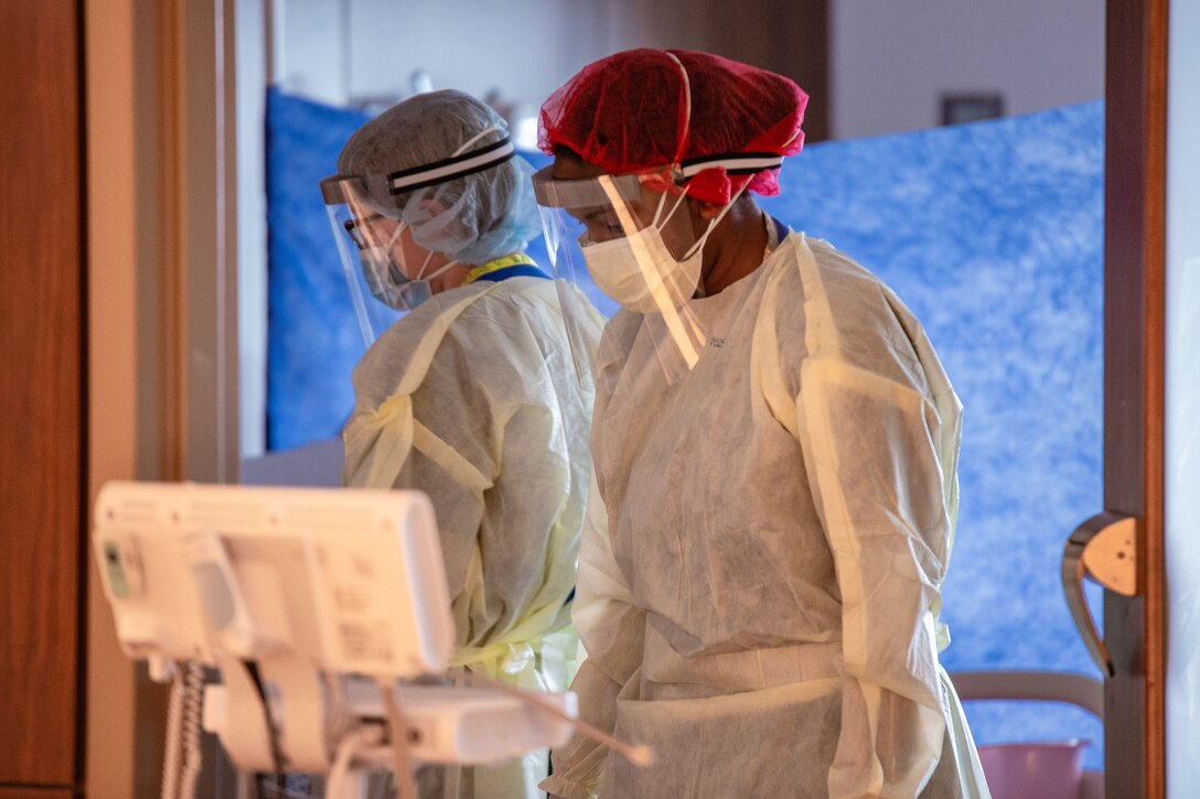 Sailors wearing full body protective gear look at patient monitors.