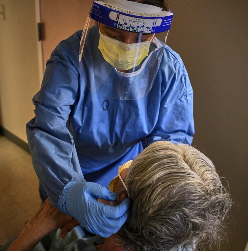 A sailor in full protective gear helps a patient put on a face mask.