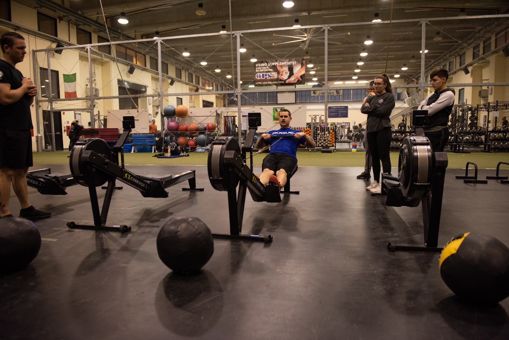 U.S. Air Force Senior Airman Eric Cooke, weapons director with the 606th Air Control Squadron and volunteer CrossFit coach, demonstrates proper rowing technique to a class at the Wyvern Fitness Center on Aviano Air Base, Italy, Feb. 26, 2020. CrossFit combines gymnastics, Olympic weightlifting, and metabolic conditioning into a single fitness sport. (U.S. Air Force photo by Tech. Sgt. Tory Cusimano)
