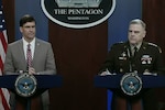 A man in a suit and an army general stand behind podiums, a Pentagon sign hanging behind them.