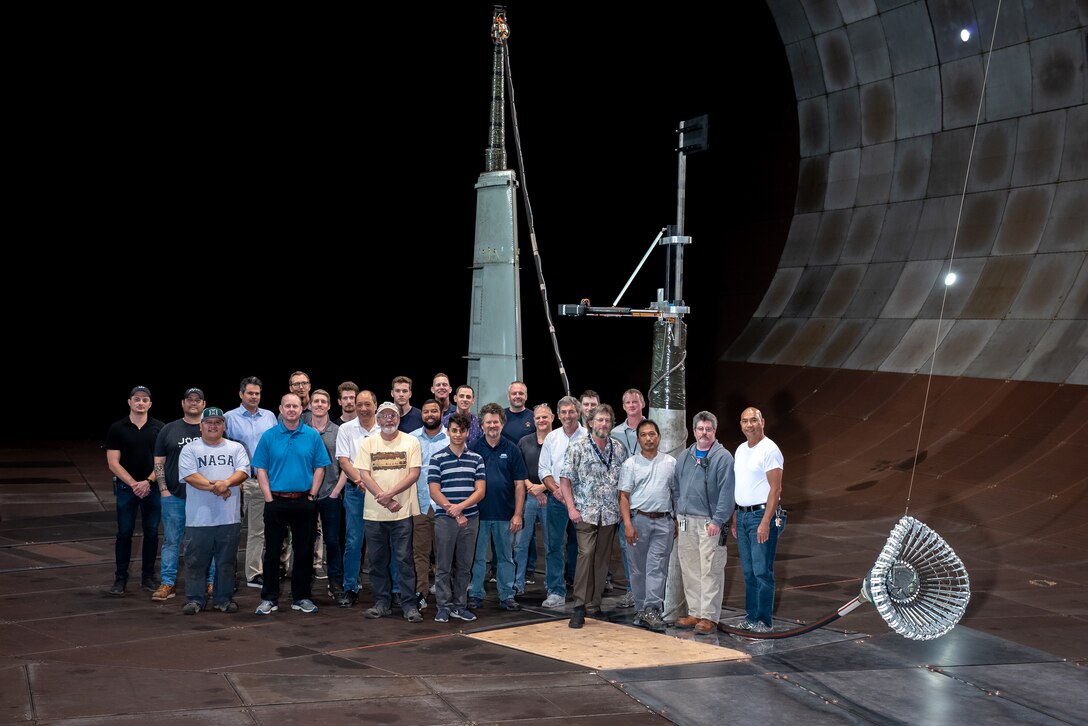 The team responsible for the testing of the integrated Actively Stabilized Refueling Drogue System and Optical Reference System stands with the tested hose and drogue system in the 40- by 80-foot wind tunnel at the Arnold Engineering Development Complex National Full-Scale Aerodynamics Complex, located in the NASA Ames Research Center at Moffett Field in Mountain View, California. The NFAC test team consisted of both Department of Defense and Test Operations and Sustainment contract employees from National Aerospace Solutions. The team included researchers, engineers, technicians and mechanics. (Courtesy photo)